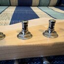 Detailní pohled na hриф kytary z jasného dřeva s viditelnou strukturou slz. Na hрифu jsou namontovány čtyři kovové ladicí mechanismy stříbrné barvy.…