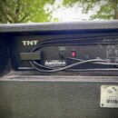 Zadní strana černého kytarového komba s povrchem z texturované syntetické kůže. Na horní části je bílý nápis TNT a vpravo schéma zapojení s označením…