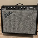 Černý kytarový kombozesilovač s šedou textilní mřížkou. Na horním ovládacím panelu jsou nápisy Princeton Reverb Amp, Fender Musical Instruments a DES…