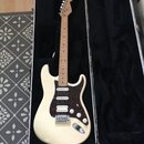 Elektrická kytara s krémovým trupem a hnědým javorovým hmatníkem v černém tvrdém kufru. Nástroj má tmavě červený pickguard, tři snímače a bílé ovláda…
