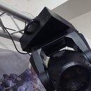 Černý pohyblivý reflektor s hranatou základnou a rukojetí, upevněný na kovovém hliníkovém trussu. Vedle něj je vidět část dalšího černého kruhového s…
