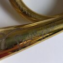 Detail zlatavého kovového trubky s rytým nápisem "L. v. Beethoven". Povrch je lesklý, s viditelnými odrazem a drobnými škrábanci. V horní části je vi…
