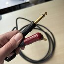 Fotografie zachycuje konec černého audio kabelu se dvěma 6,3mm jack konektory. Jeden konektor je černý a druhý červený, oba mají zlatý povrch hrotu a…