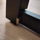 Detailní záběr na spoj černého dřevěného nebo laminovaného nábytku, pravděpodobně stojanu. V místě spoje dvou hran je viditelný výrazný odryv povrcho…