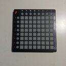 Černý MIDI kontrolér s mřížkou 8x8 podsvícených bílých políček. Na pravém okraji je svisle napsáno LAUNCHPAD MINI a níže logo novation. V horní části…
