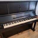 Černé akustické piano s klaviaturou z bílých a černých kláves. Na přední části nad klaviaturou je nápis AKORD v oválném rámečku a v horní části korpu…