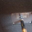 Detail zadní strany černého reproduktorového boxu s kovovým štítkem. Na štítku je uveden text SERIAL W0906B05103614, MODEL 410BLX II, IMPEDANCE 8 OHM…