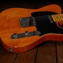 Elektrická kytara typu Telecaster v žlutohnědé barvě s černým pickguardem. Nástroj má javorový hmatník a kovové ovládací prvky. Povrch těla vykazuje…