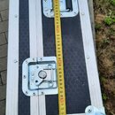 Hliníkový přepravní kufr s černým povrchem a texturovanou strukturou. Na kufr je položen žlutývstupní metr, který ukazuje délku přes 80 cm. Viditelná…