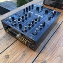 Černý DJ mixér s mnoha ovládacími knoflíky, posuvníky a tlačítky. Na přední hraně je bílý nápis Pioneer DJ a označení modelu XDJ-R1. Zařízení má v za…