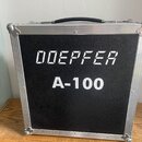 Černý transportní kufr s hliníkovým profilem a kovovými rohy. Na čelní straně je bílý nápis „DDEPFER A-100“. Povrch kufrů vykazuje mírné opotřebení v…