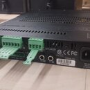 Zadní strana černého elektronického zařízení s několika konektory. Jsou zde tři zelené šroubovací svorkovnice a nápisy SPEAKER, WIRING, IN 1, IN 2 a…