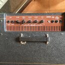 Černý kytarový kombo zesilovač s texturovaným povrchem a hnědým ovládacím panelem. Na panelu jsou nápisy INPUT, VOLUME, TREBLE, HIGH-MID, LOW-MID, BA…