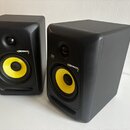 Dva černá studiová monitorovací reproduktory s žlutými membránami basových reproduktorů. Na obou je vidět logo KRK a nápis Rokit 5. Povrch skříní je…