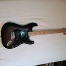 Elektrická kytara s tmavým, gradientním povrchem těla a černým pickguardem. Na hlavě hmatníku je nápis Squier STRATOCASTER. Nástroj má tři snímače, z…