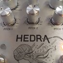 Detailní záběr na stříbrný kovový panel efektového pedálu. Na panelu jsou vidět stříbrné oválné knoflíky s nápisy PITCH 1, PITCH 2 a PITCH 3. Uprostř…
