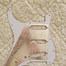 Bílá pickguard pro elektrickou kytaru s připevněnou hliníkovou stínící vrstvou. Hliníková fólie vykazuje výrazné pomačkání, rýhy a nerovnoměrné nalep…