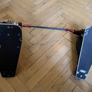 Dvojpedál na bicí buben v černé barvě s kovovými komponenty. Pedály mají černé povrchy a jsou spojeny kovovou tyčí s červenými spojovacími prvky. Nás…