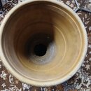 Fotografie zachycuje pohled shora do vnitřku hliněného, kuželovitého předmětu s okrouhlým otvorem na dně. Povrch je v přirozené hnědožluté barvě s vi…