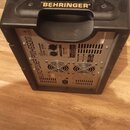 Černý zesilovač v plastovém pouzdře s úchytem, na kterém je žlutý nápis BEHRINGER. Na zadním kovovém panelu je svisle napsáno EUROPOWER PPH600. Jsou…