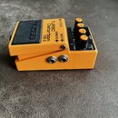 Kytarový efekt pedál v oranžovém kovovém provedení. Na horní části je černý spínací pedal s nápisem BOSS a ovládací panel s texty TURBO distortion DS…