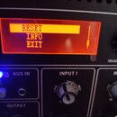 Detailní záběr na ovládací panel černého elektronického zařízení. V horní části je červeně podsvícený displej s oranžovým textem RESET, INFO a EXIT.…