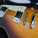 Detailní pohled na elektrokitaru s trupem v barevnosti sunburst a krémovým pickguardem. Na těle jsou dva humbuckery s krémovými rámečky, chromovaný k…