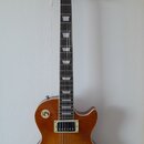 Elektrická kytara s trupem z dřeva v medově hnědé barvě a tmavým hmatníkem. Na hlavě je bílý nápis Gibson a pod ním menší text, který není čitelný. N…