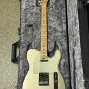 Elektrická kytara typu Telecaster v krémové barvě s bílým pickguardem, umístěná v černém tvrdém kufru s šedou plišovou výstělkou. Na hlavě hmatníku j…