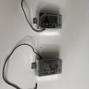 Dvě chromované snímače pro elektrickou kytaru s kovovými kryty a viditelnými šrouby. Každý snímač má připojený šedý opletený kabel s odhalenými vodič…