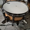 Fotografie zobrazuje buben (snare) s přírodním dřevěným povrchem a chromovaným obručováním. Na bílém blátci jsou vidět nápisy „TAMA POWER CRAFT“ a „T…
