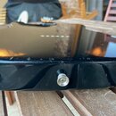 Detailní pohled na černý lakovaný bok a hranu těla elektrické kytary. Na horní hraně jsou vidět četné škrábance a odřeniny laku. V boku je umístěn ko…