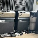 Dvě kytarové komba značky Fender umístěná na dvou černých kytarových boxech značky Laney. Komba mají stříbrný přední panel s nápisy Fender a v pravém…