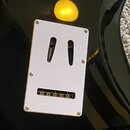 Detail zadní strany černé elektrické kytary s bílým plastovým krytem elektroniky. Kryt je připevněn čtyřmi šroubky a obsahuje dva oválné výřezy pro p…