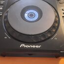Černý digitální DJ player značky Pioneer s velkým ovládacím jog kola. Na spodní části je bílý nápis Pioneer a v pravém dolním rohu označení MULTI PLA…