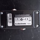 Zadní strana černého efekt pedálu z plastu nebo kovu. Na bílém štítku je uveden nápis tc electronic, DESIGNED IN DENMARK, E80002111, N1839 a 9V DC/10…