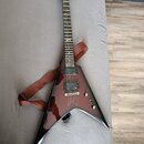 Elektrická kytara s agresivním V-tvarem v tmavě červeném průsvitném lakování. Na hmatníku je viditelné logo značky Jackson. Kytara má dva humbuckery,…