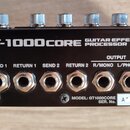 Zadní strana černého efektového procesoru s nápisem BOSS GT-1000CORE GUITAR EFFECTS PROCESSOR. Jsou zde vidět vstupy a výstupy s označením INPUT R/MO…