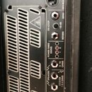 Detail zadní strany kytarového komba s černým povrchem a ventilační mřížkou. Jsou zde vidět konektory s nápisy SPEAKERS (2 X 8 OR 1 X 4 OHMS, 8-16 OH…