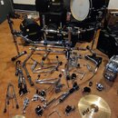 Sada komponentů bubnové soupravy a činelů rozložená na hnědé podlaze. Jsou zde černý basový buben a tom s nápisy HARDCASE, chromovaný hardware v podo…