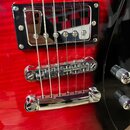Detail červené elektrické kytary s výraznou strukturou dřeva. Je vidět chromovaný humbucker v černém rámečku, Tune-o-matic kobylka a stopbar strunník…