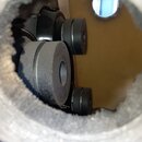 Fotografie zachycuje pohled skrz otvor do vnitřku akustického nástroje. Uvnitř jsou vidět tři černé, válcovité součástky z matního materiálu s otvore…