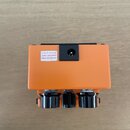 Detailní pohled na zadní stranu oranžového efekt pedálu. Na černé plastové části je bílá nálepka s nápisem USE BOSS PSA ADAPTOR ONLY (DC 9 V) a symbo…