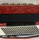Červená akordeon s povrchem v optice mramoru. Na přední straně je bílý panel s černými knoflíky a nápis romance. Mezi knoflíky a vrchní částí je čern…