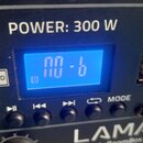 Detail ovládacího panelu černého audio zařízení s nápisem POWER: 300 W a značkou LAMAX RoomBox 300. Panel obsahuje modrý digitální displej, slot pro…