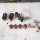 Sada černých snímačů pro elektrickou kytaru, zahrnující dva úzké a jeden širší snímač s viditelnými zlatými póly. Součástí jsou čtyři červeně hnědé p…