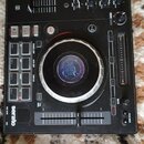 Černý DJ kontrolér s velkým kruhovým jog-wheelem a centrálním displejem. Na zařízení jsou viditelné nápisy serato, SYNC, CUE, SAMPLER a označení fade…