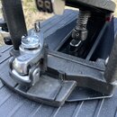 Detailní pohled na černý mechanismus bicího pedálu. Na kovovém členu je viditelné vyryté logo znázorňující stylizované písmeno S v rámečku. Povrch če…