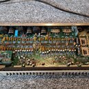 Fotografie zachycuje vnitřek elektronického zařízení v kovovém šasi. Na zelené základní desce jsou rozmístěny kondenzátory, rezistory a integrované o…
