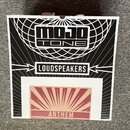 Fotografie znázorňuje horní stranu černé krabice s bílými grafickými prvky. Na krabici je uveden nápis MOJO TONE, slovo LOUDSPEAKERS a v červeném rám…